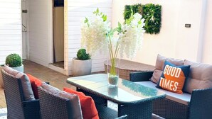 Un espace extérieur aménagé avec des meubles en osier, une table en verre et un coussin orné de l'inscription « GOOD TIMES ».