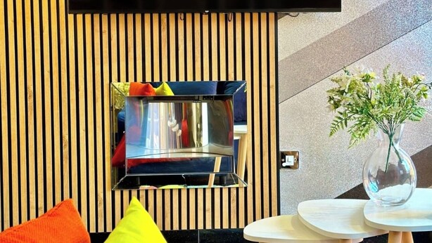 Un salon moderne doté d’un grand téléviseur à écran plat fixé à un mur en bois, d’une cheminée intégrée et d’une petite table sur laquelle est posé un vase de fleurs.
