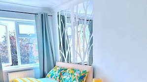Une chambre à coucher moderne avec un lit, une chaise, une lampe et une fenêtre avec des rideaux.