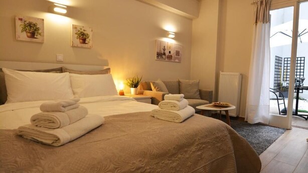 A hotel room with a large bed, a small sofa, a table with a plate, and a view of the outside through a window.