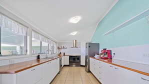Une cuisine moderne avec des meubles blancs, une hotte en acier inoxydable, une machine à café rouge et une fenêtre ornée de rideaux en dentelle.