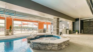 En indendørs swimmingpool med et boblebad, stensøjler og udsigt til det fri.