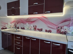 Eine moderne Küche mit Spüle aus Edelstahl, einer weißen Arbeitsplatte und einer Spritzschutzwand mit floralem Muster.