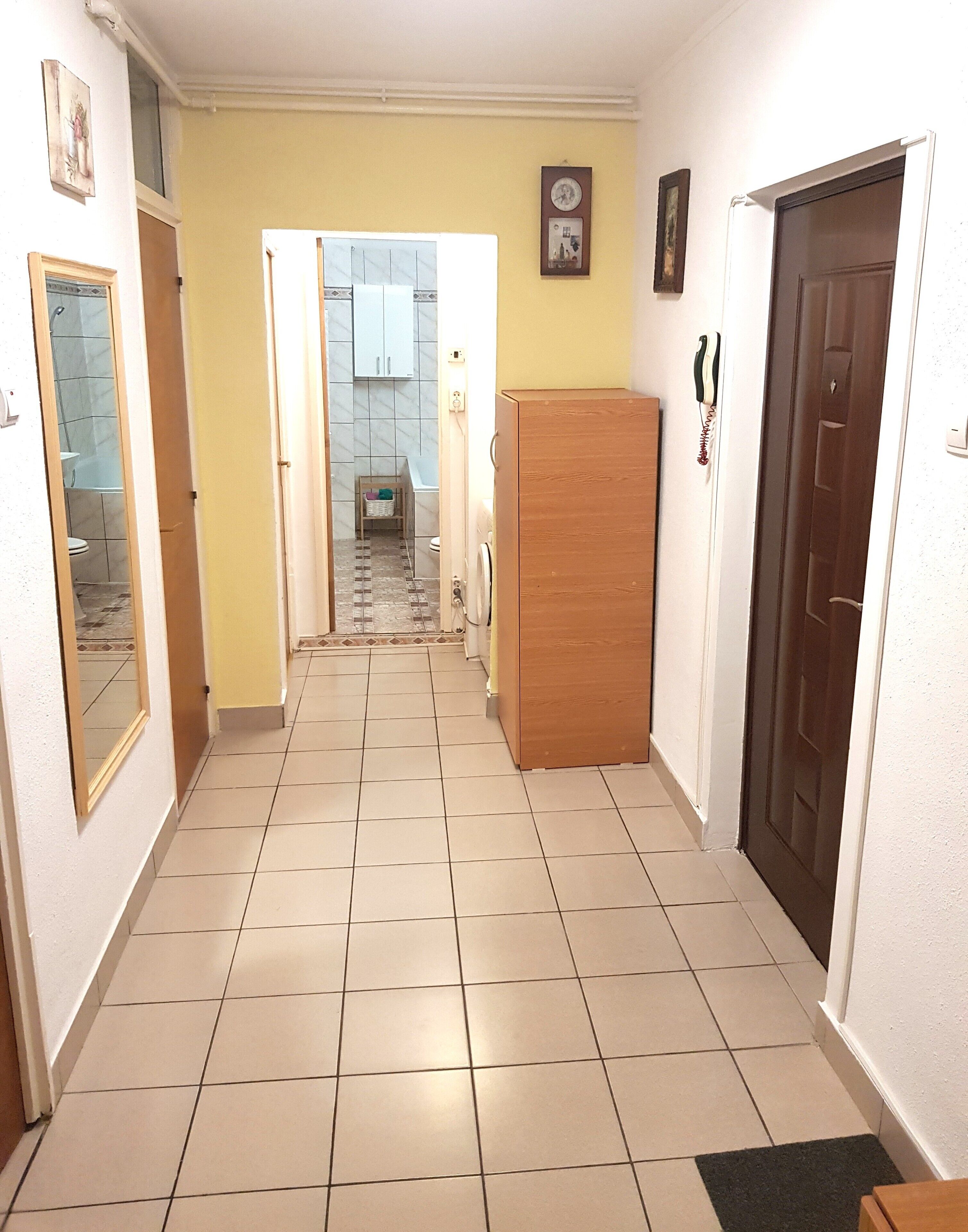 A hallway with a tiled floor, a wooden door on the right, and a mirror on the left.