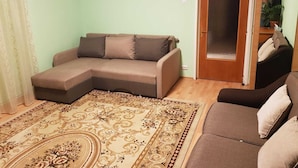 A living room with a sectional sofa, a patterned rug, a door with a mirror, and a small plant on a shelf. - Central Apartment Bucharest - Vitan Mall (Bucuresti)