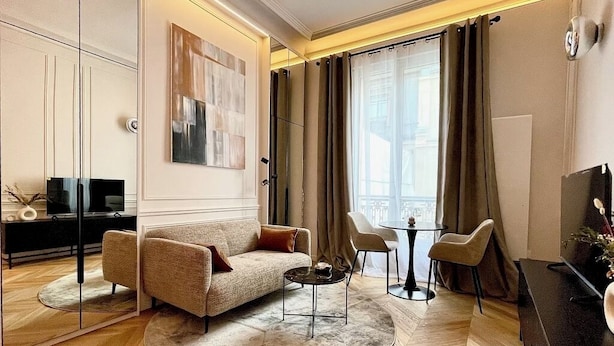 Un salon moderne comprenant un canapé, une table basse et des fauteuils, un téléviseur et une grande fenêtre avec des rideaux.