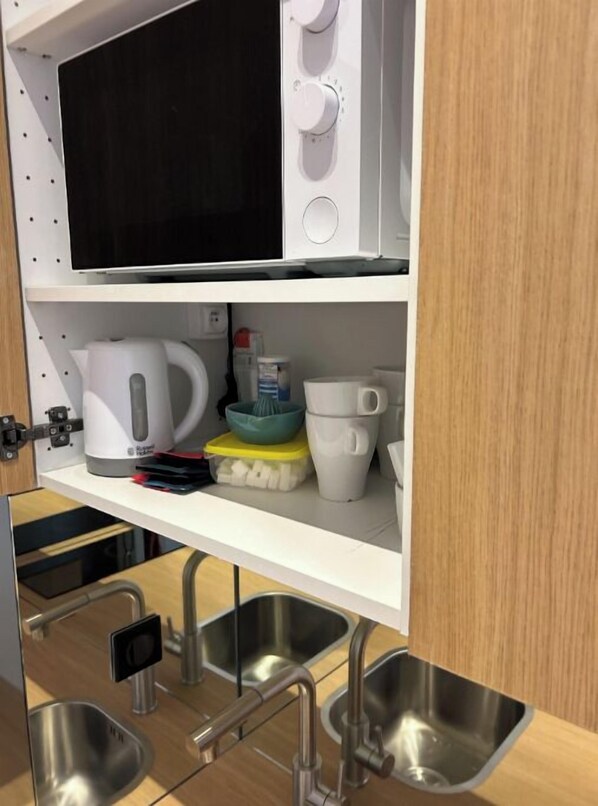 A kitchen with a microwave, kettle, and various utensils on the countertop.