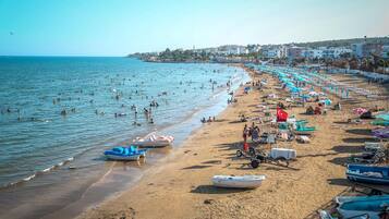 Een strand met veel mensen die zwemmen en zonnebaden, boten en strandparasols.