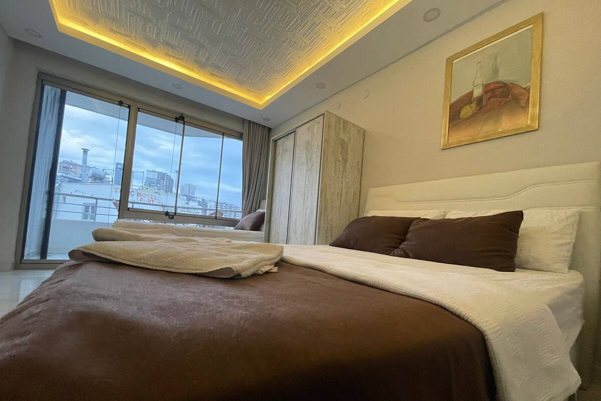 Habitación de hotel moderna con una cama grande, vista a la ciudad a través de la ventana y un diseño de iluminación único en el techo.