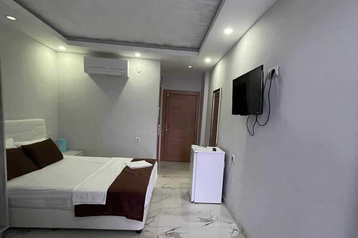 Habitación de hotel con cama, refrigerador pequeño, televisor montado en la pared y puerta que da a otra habitación.