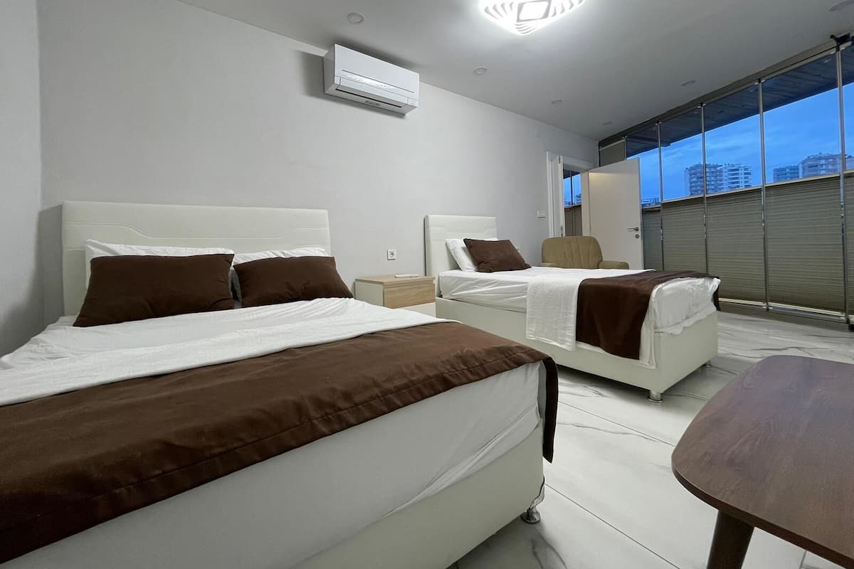 Una habitación de hotel moderna con dos camas, un ventanal grande con vista a la ciudad y un equipo de aire acondicionado en la pared.
