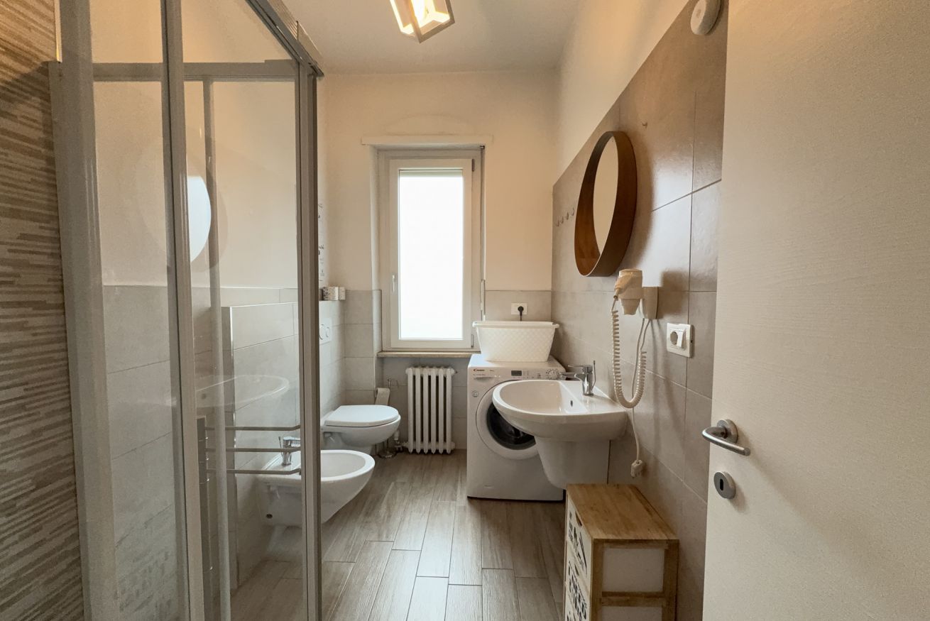 Une salle de bain avec une douche à parois de verre, des toilettes, un lave-linge, un lavabo et un miroir.
