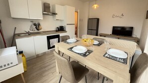 Une cuisine compacte avec des meubles blancs, une table à manger pour quatre personnes et un téléviseur posé sur un meuble.