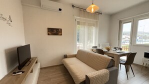 Un salon moderne avec un canapé, un téléviseur, une table à manger avec des chaises et une grande fenêtre.