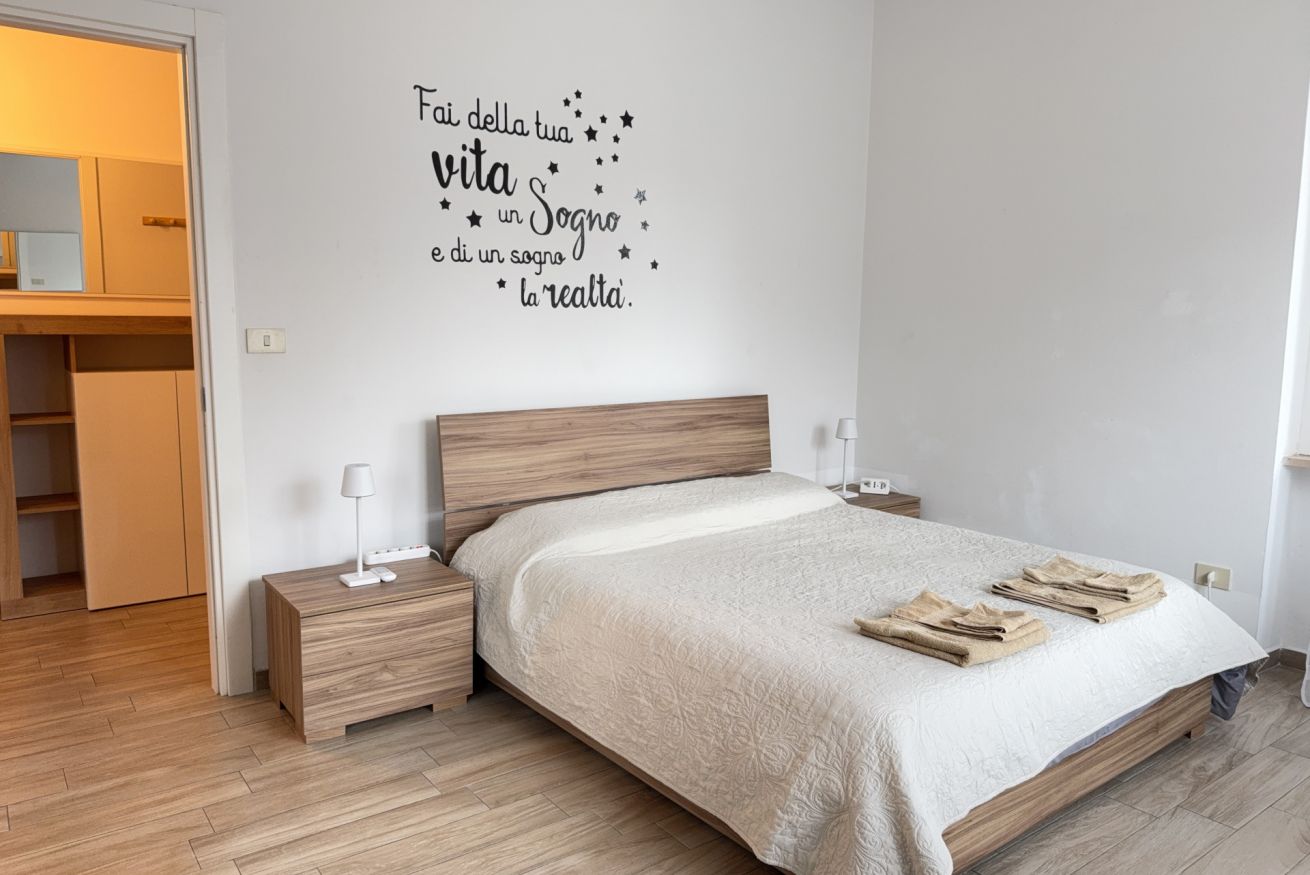 Une chambre à coucher avec un lit en bois, des tables de chevet, une commode, une armoire et un mur orné d’une citation inspirante.