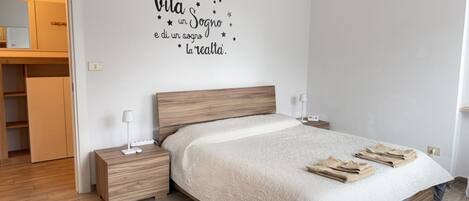 A bedroom with a wooden bed, bedside tables, a nightstand, a wardrobe, and a wall with a motivational quote.