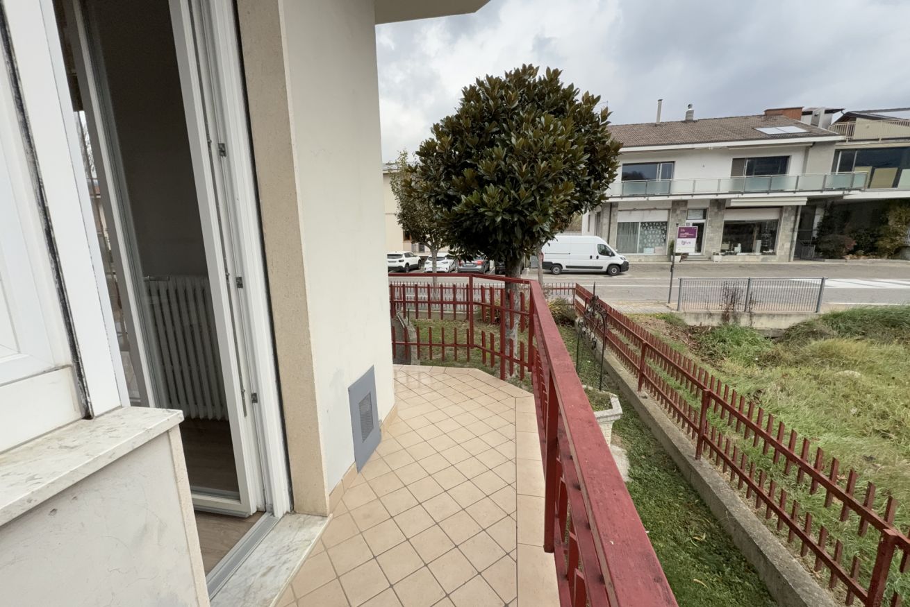 Un balcone con pavimento piastrellato, ringhiera rossa e un albero.