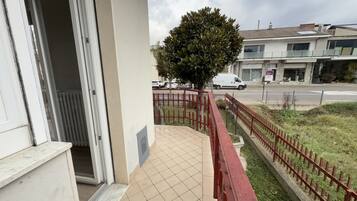 Un balcone con pavimento piastrellato, ringhiera rossa e un albero.