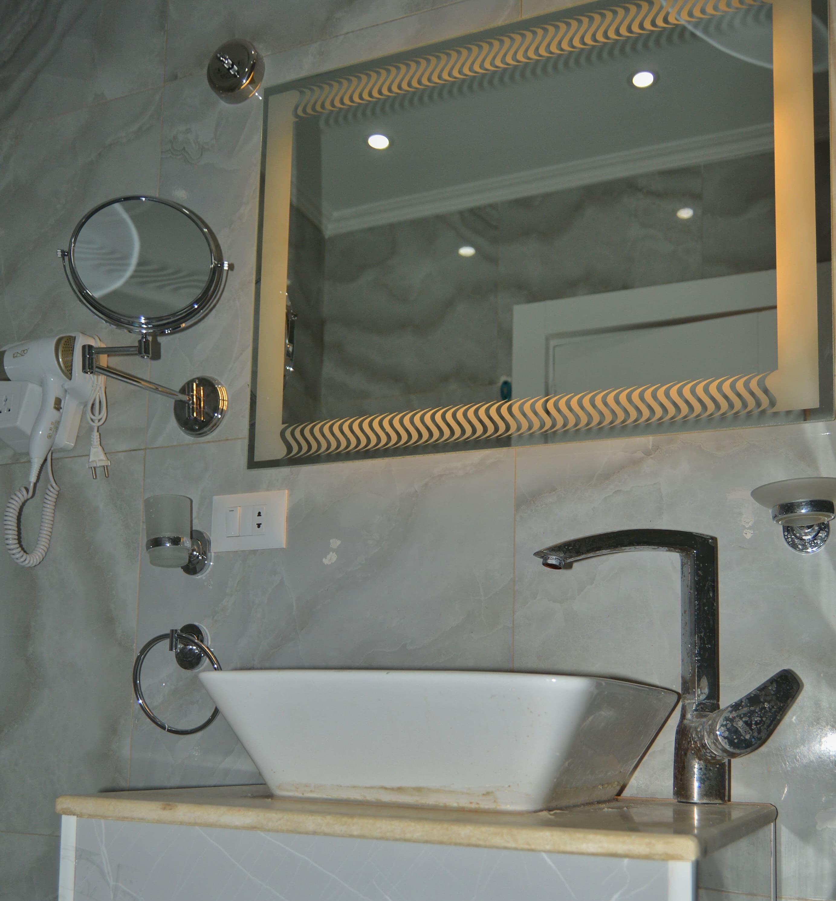 Une salle de bain avec un lavabo blanc, un miroir et un sèche-cheveux portatif.
