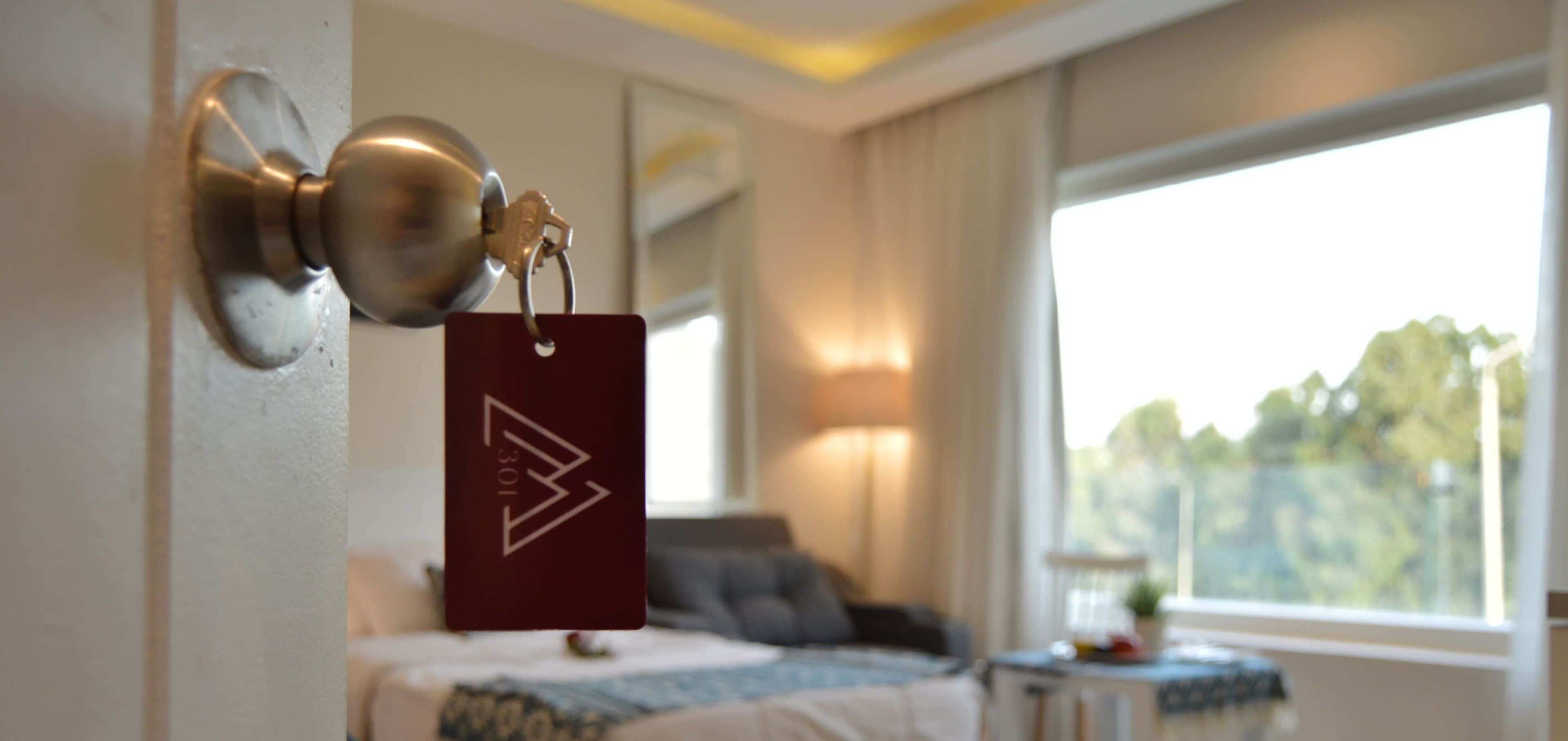 A hotel room with a bed, a nightstand, a lamp, and a window with a view of trees.