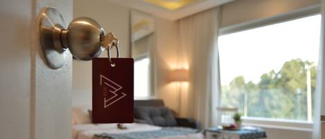 A hotel room with a bed, a nightstand, a lamp, and a window with a view of trees.