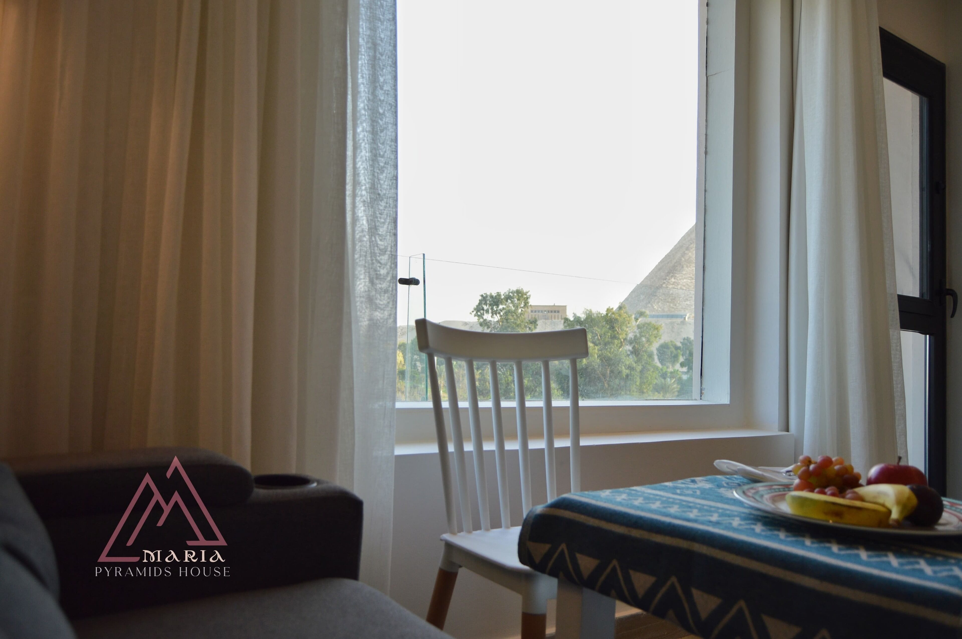 A room with a view of a mountain, a white chair, a table with a fruit plate, and a logo on the wall.