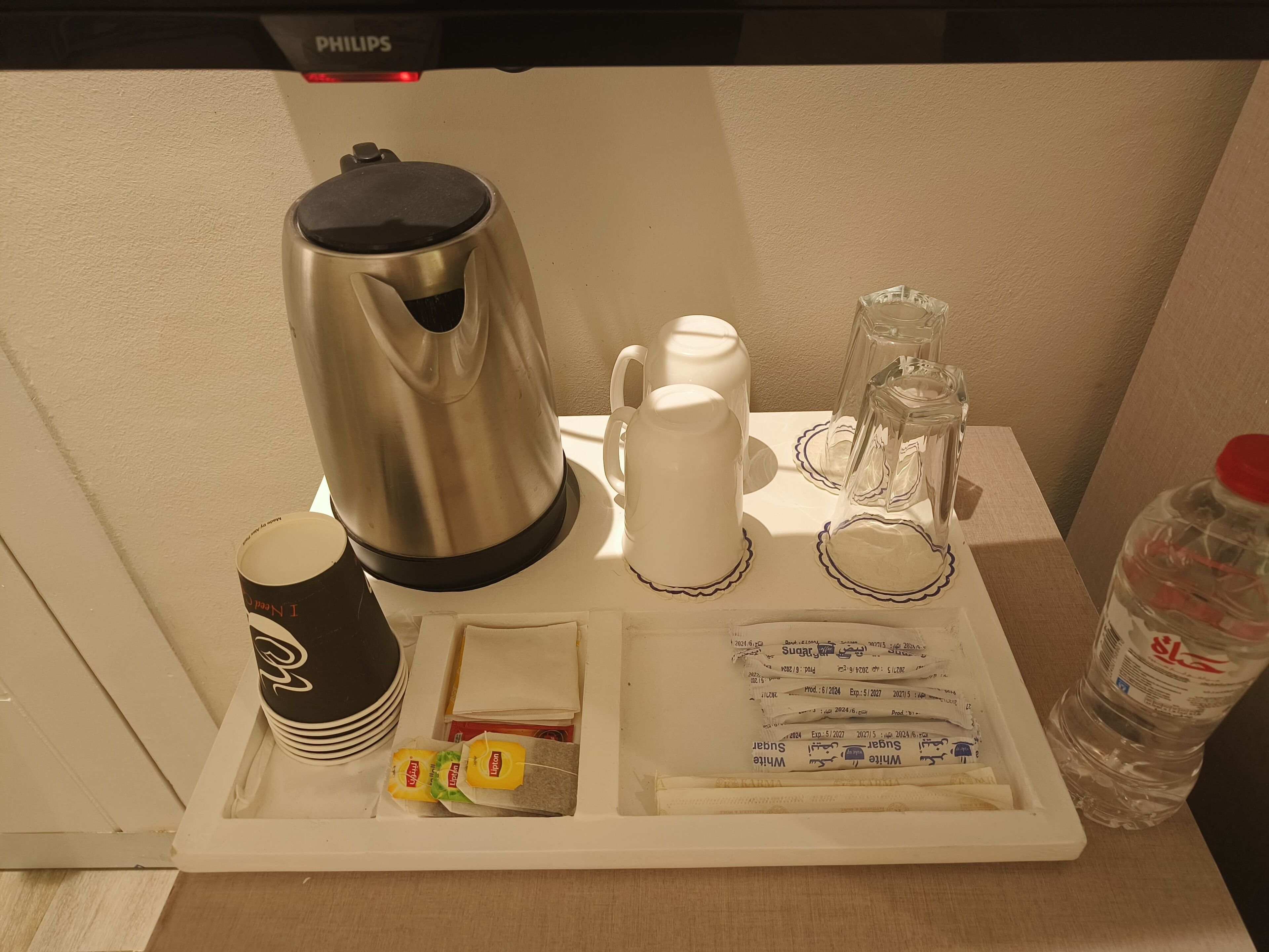 A tray with a coffee maker, cups, sugar packets, and a water bottle.