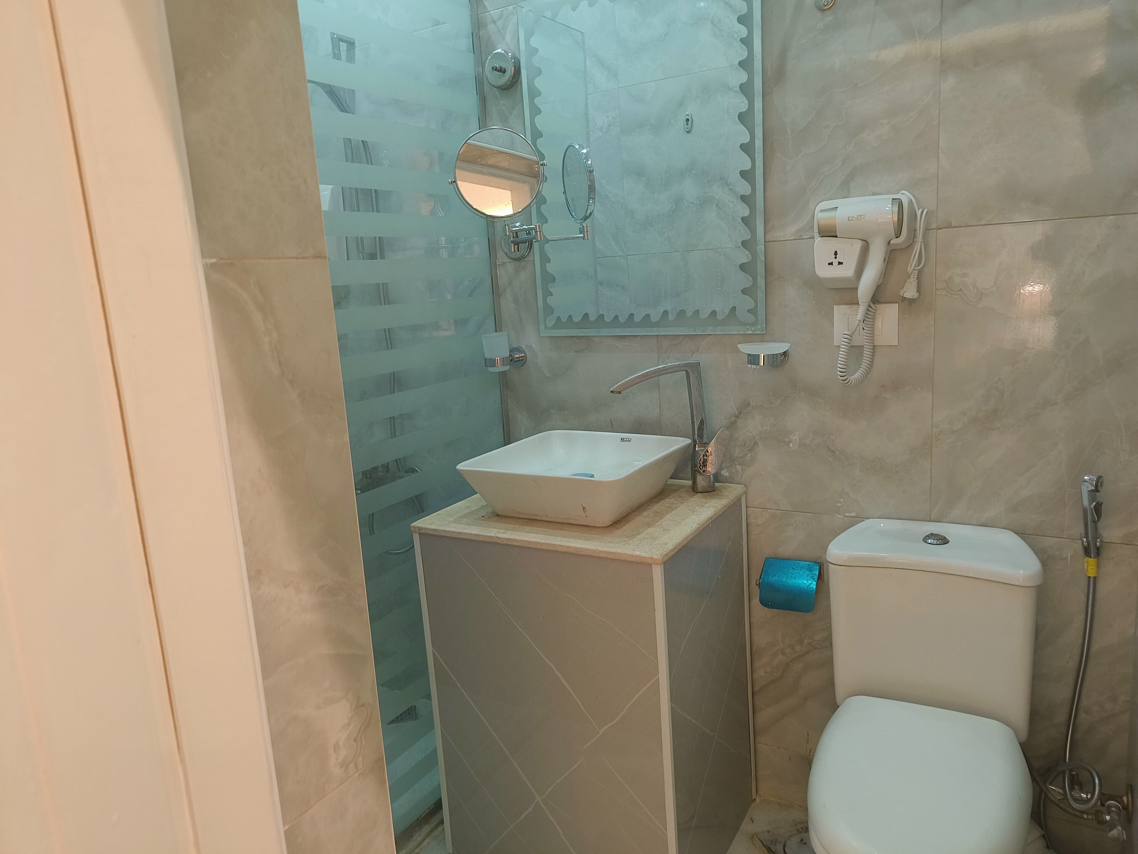 A bathroom with a glass shower enclosure, a sink, a toilet, and a mirror.