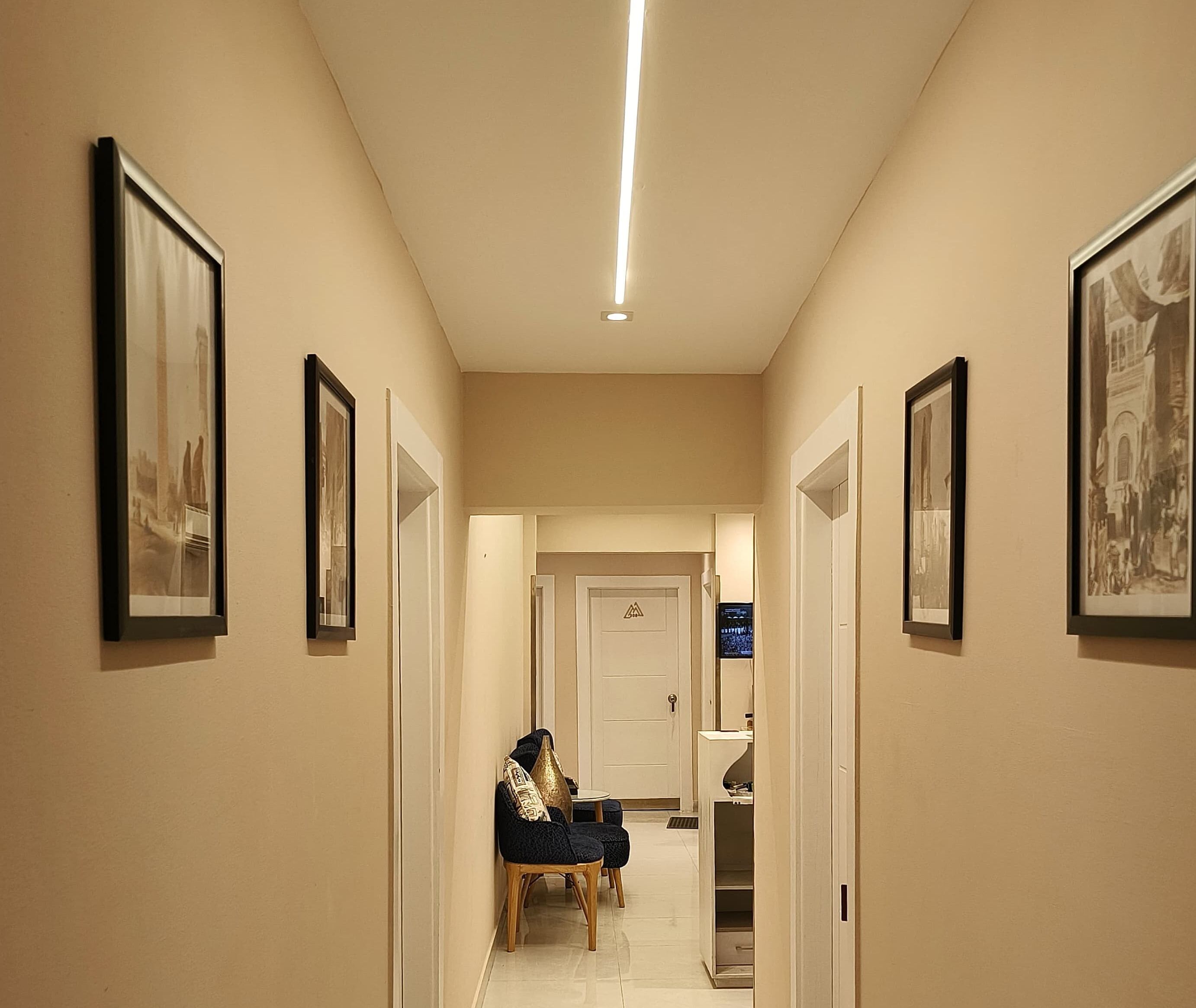 A hallway with framed pictures on the walls, a door at the end, and a small table with chairs in the center.