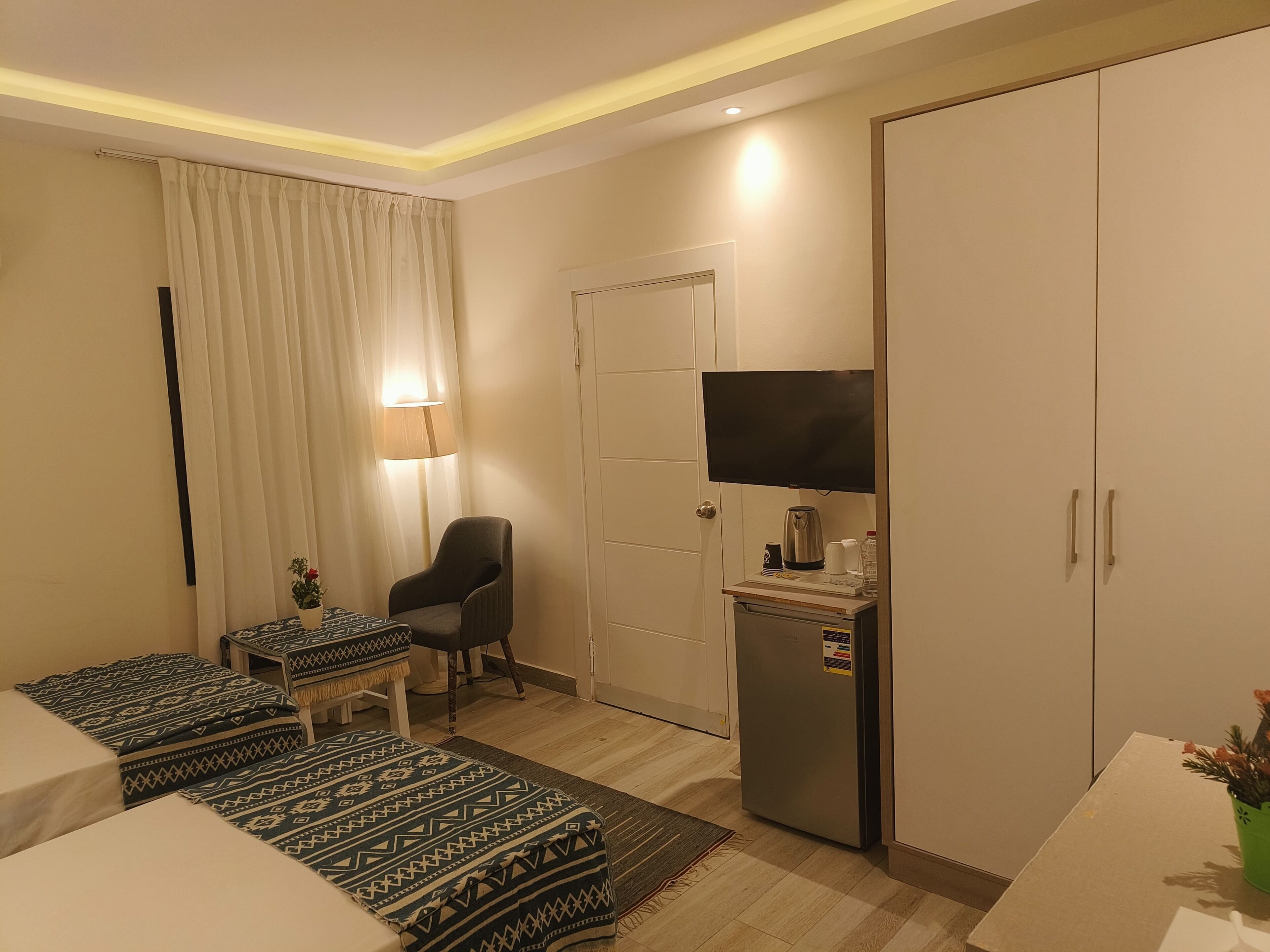 Habitación de hotel con cama, escritorio, silla, televisor, refrigerador y armario.