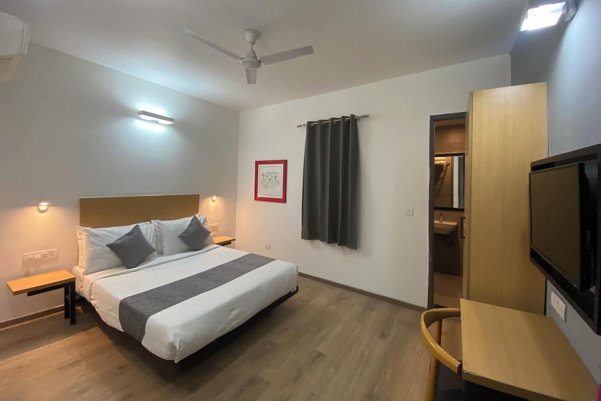 Ein Hotelzimmer mit Bett, Nachttischen, Deckenventilator, gerahmtem Bild an der Wand und Fernseher.