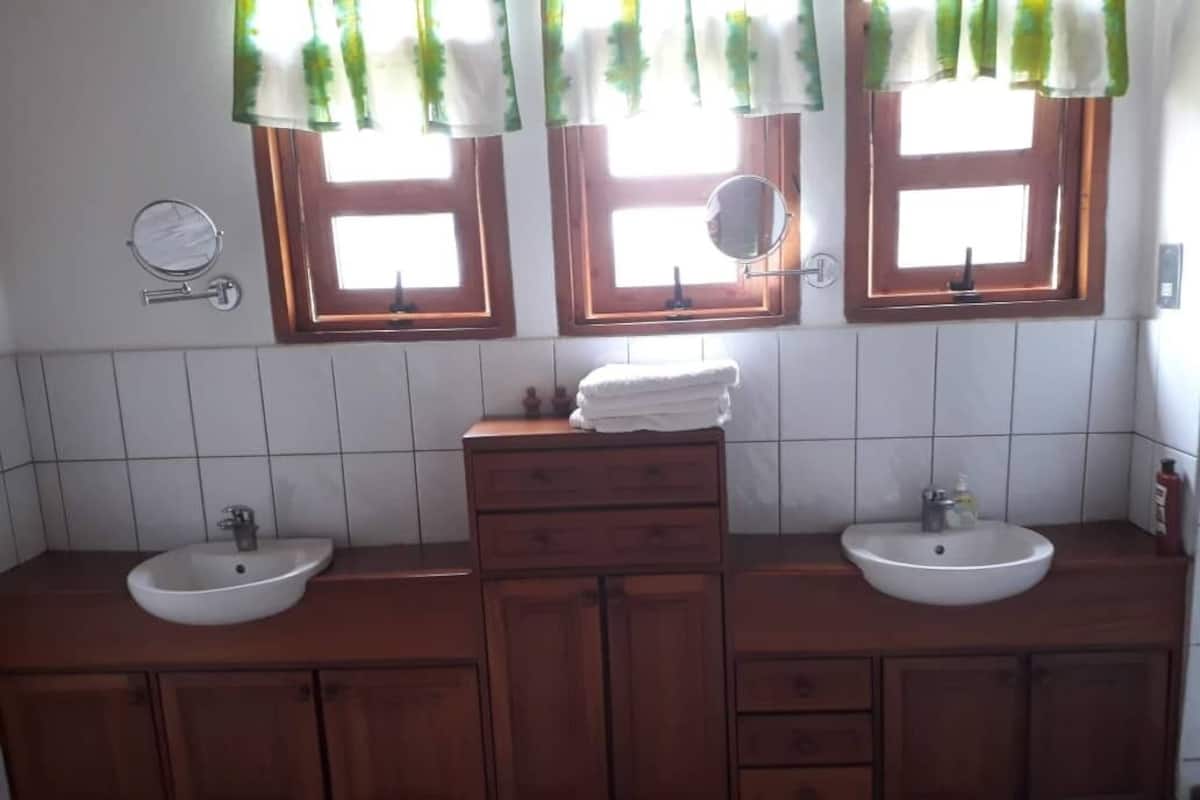 Kylpyhuoneessa on kaksi pesuallasta, puukaapit ja peili jokaisen ikkunan yläpuolella.