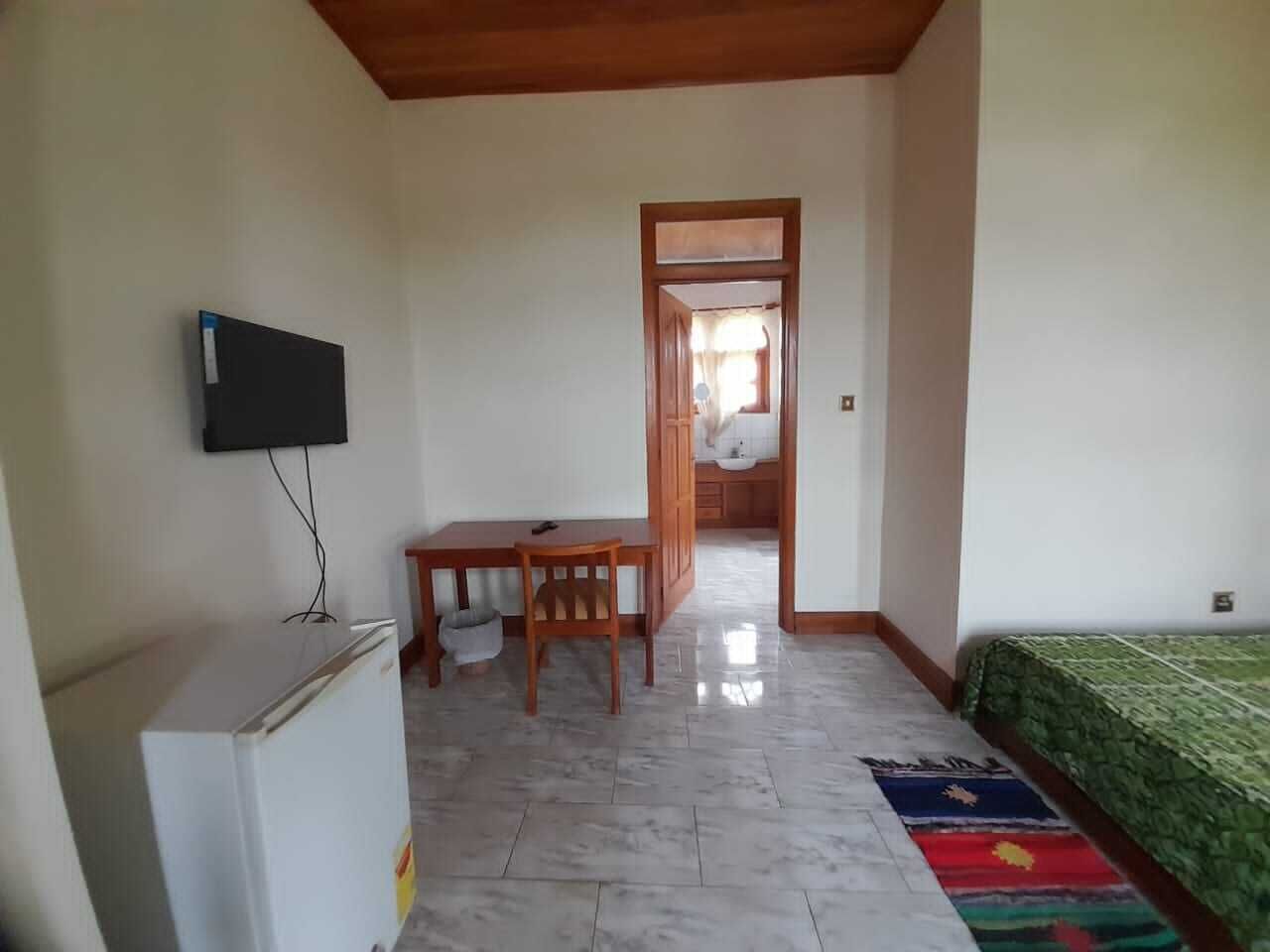 Una habitación con una cama, un escritorio, una silla, un televisor y un refrigerador.