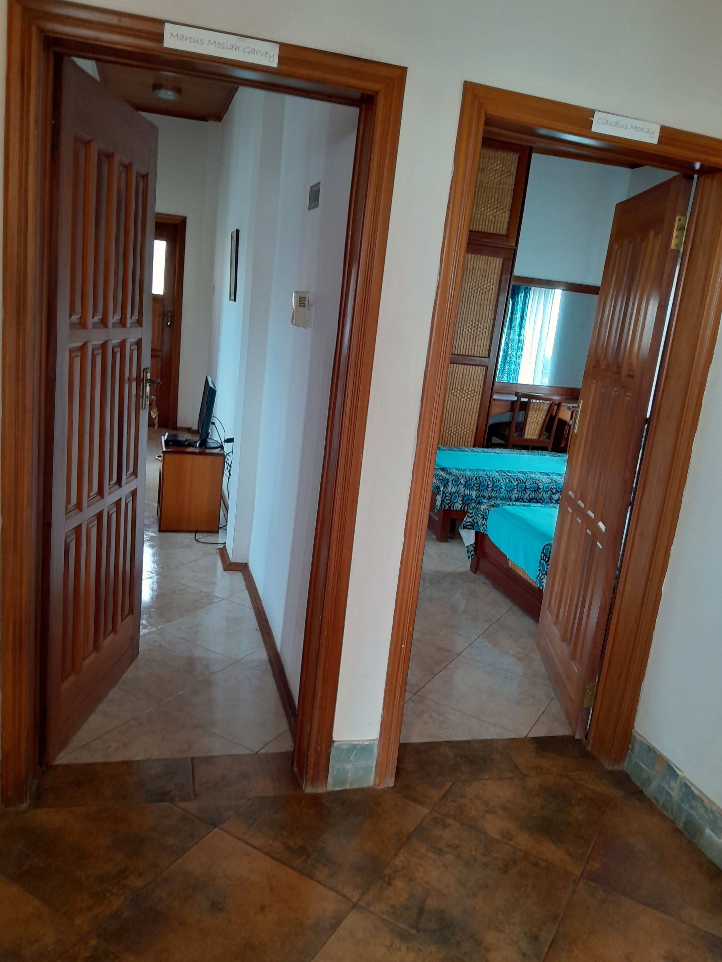 Um corredor com uma porta de madeira que dá para um quarto com uma cama e uma escrivaninha.