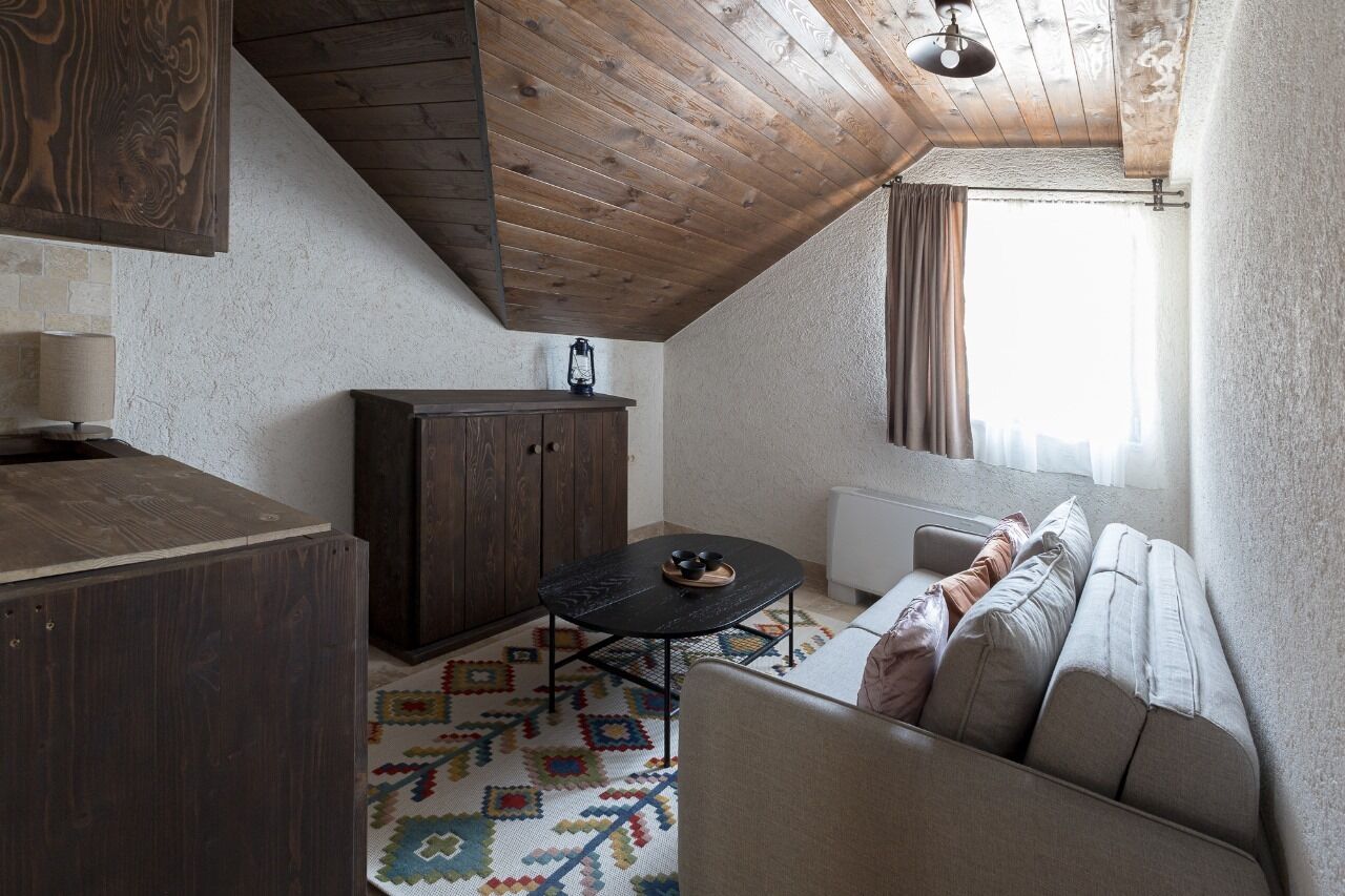 Una habitación cálida en el ático, con techo de madera, un sofá, una mesita y un armario.