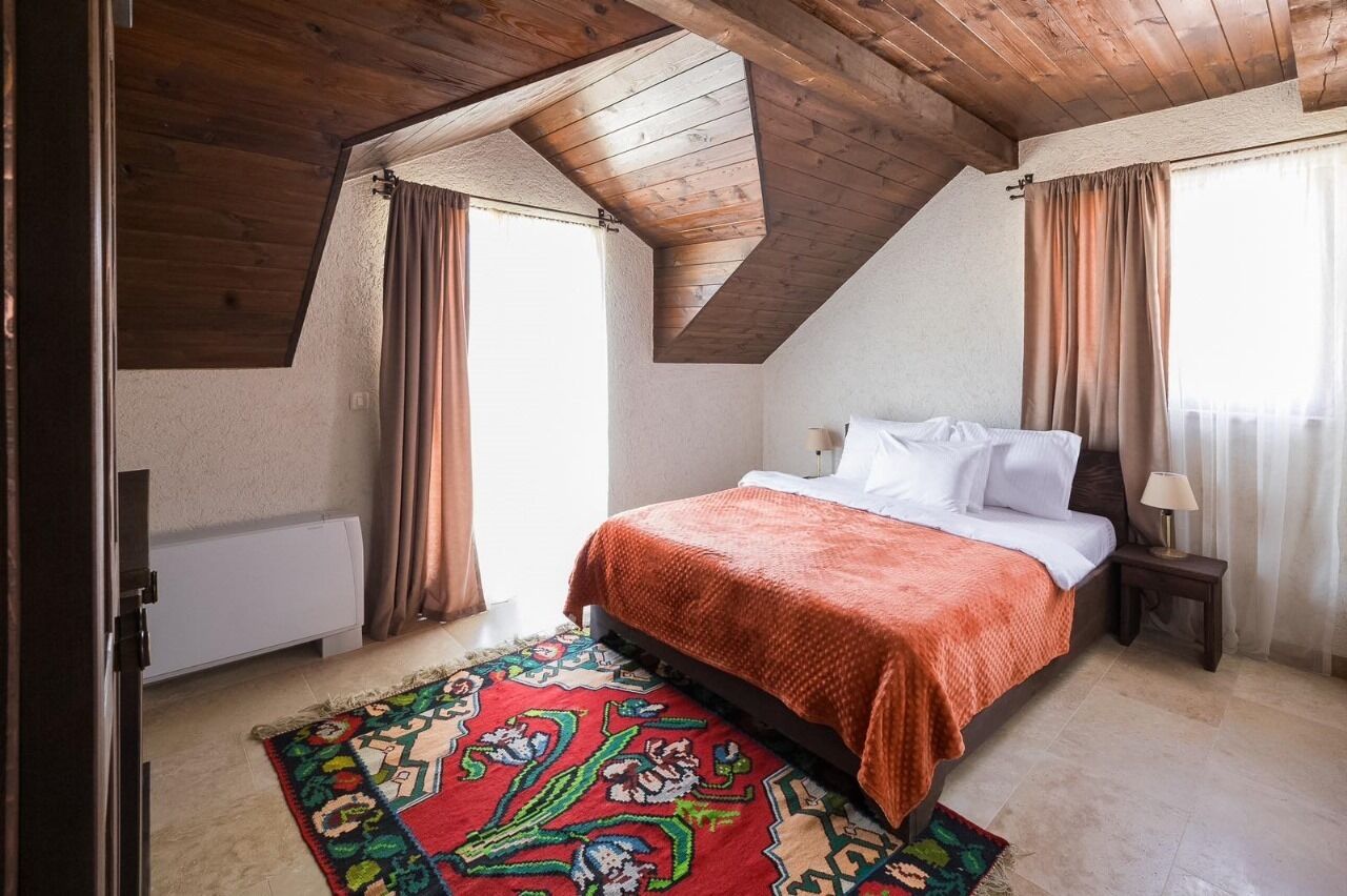 A bedroom with a sloped ceiling, a bed with white linens, a patterned rug, and a nightstand with a lamp.