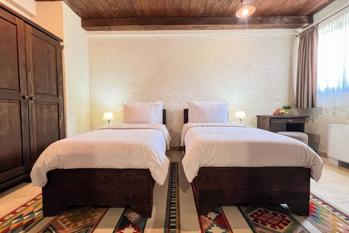A bedroom with two beds, wooden wardrobe, and a small table with fruit.