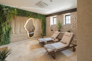A spa room with two sun loungers, a stone wall, and a green wall with plants. - Bistrička Čaršija Hotel & SPA (Bistrica)