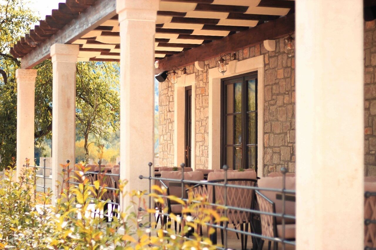 Un patio al aire libre con columnas de piedra, asientos acolchados y una pérgola.