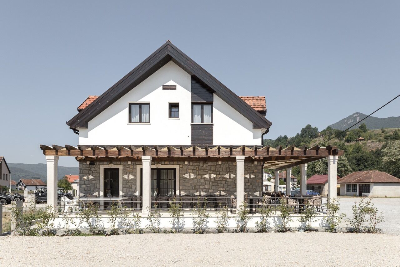 A two-story house with a stone facade, a covered porch, and a mountain backdrop.