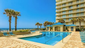 A pool area with lounge chairs, a pool, and a building with balconies.