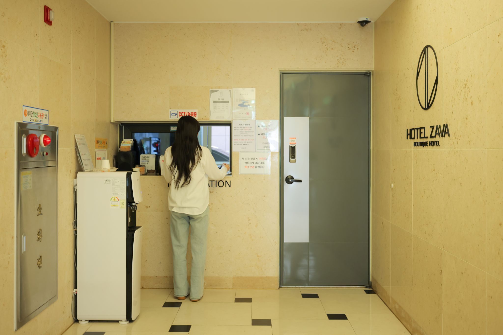 A hotel reception area with a reception desk, a security camera, a refrigerator, and a door with a lock.