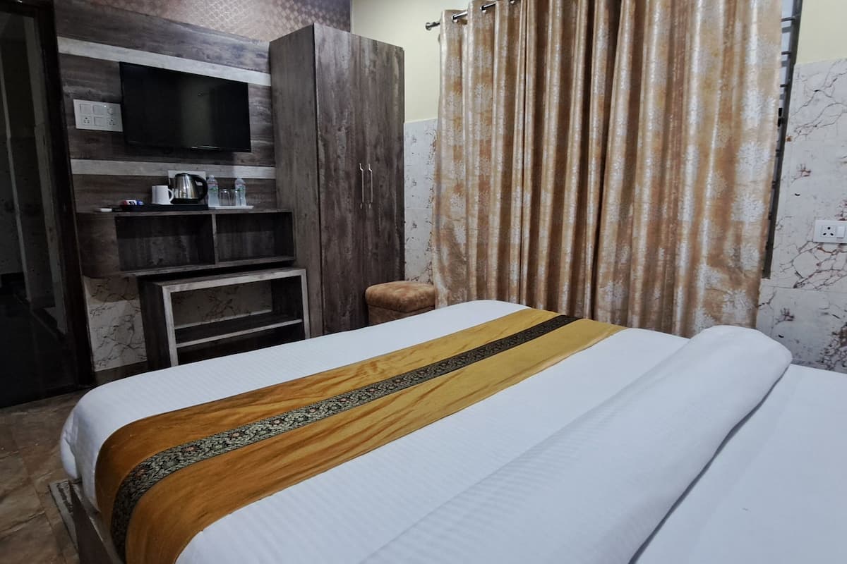 A hotel room with a bed, a TV mounted on the wall, a wardrobe, and a small table with a kettle and cups.