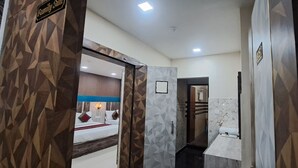 A hotel hallway with a geometric patterned wall, a bed with red and white bedding, and a bathroom with a marble vanity. - RS Residency By Wheels Hospitality (Varanasi)