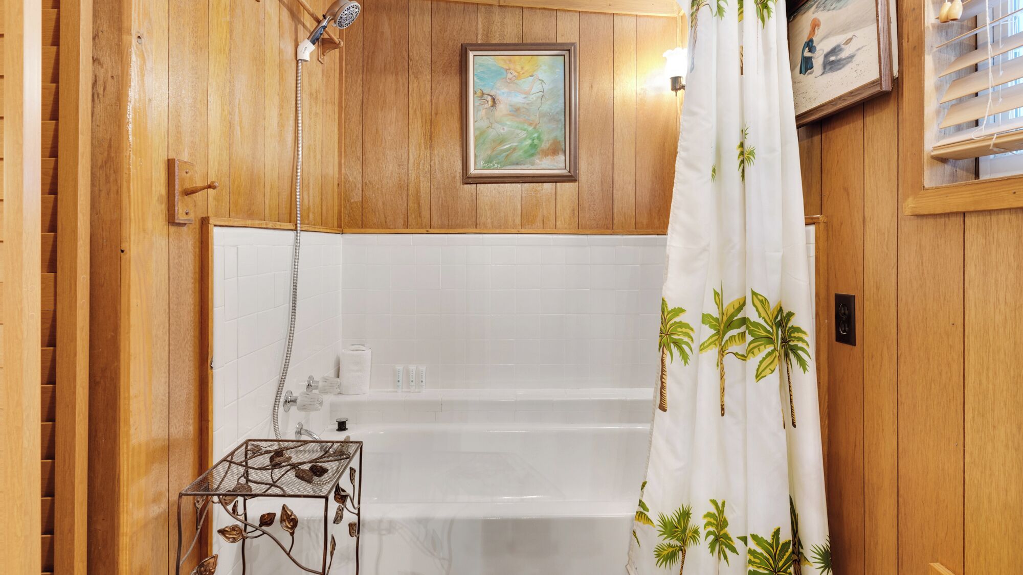 Casa de banho de madeira com chuveiro, um quadro emoldurado e uma mesa de metal com motivos florais.