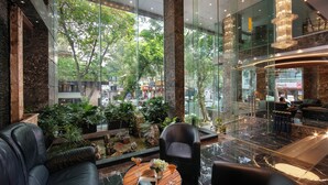 A modern lobby with a glass wall, leather seating, a wooden table with drinks, and a chandelier. - May De Ville Corner Hotel (Hanoi)