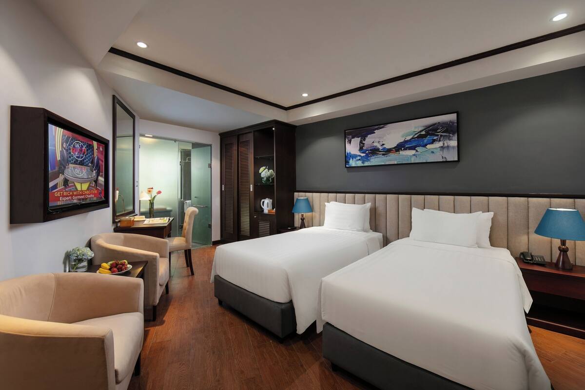 A hotel room with two beds, a desk, a chair, and a TV.