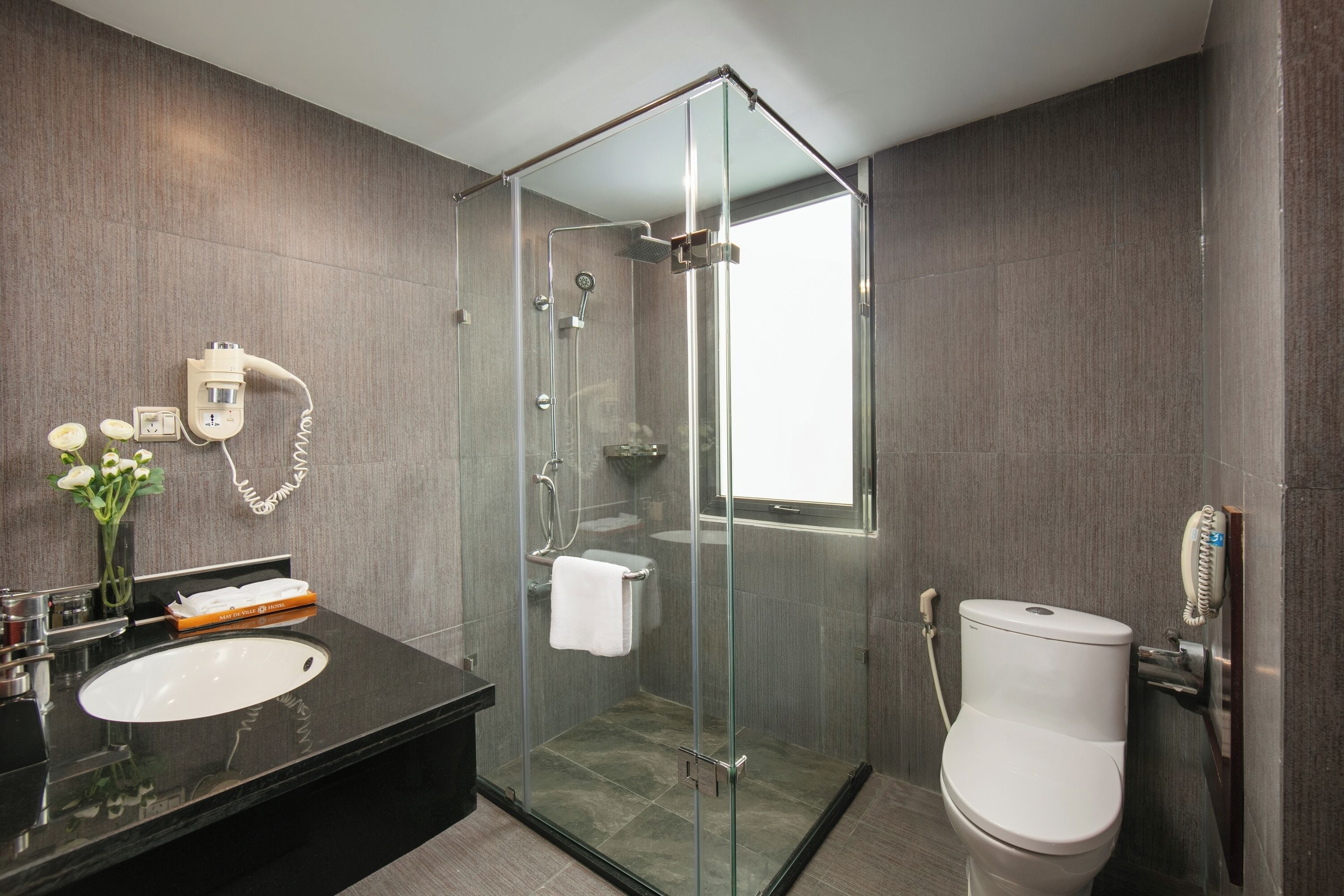 A modern bathroom with a glass-enclosed shower, a white toilet, and a black sink.