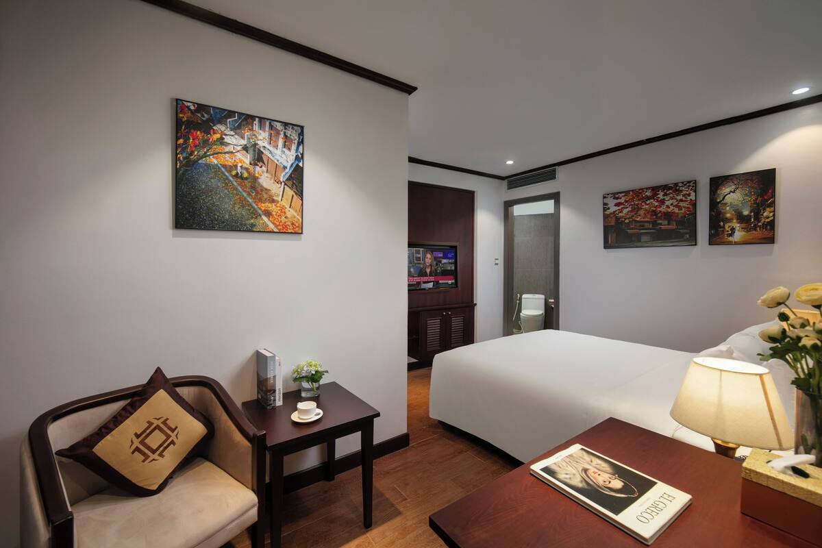 A hotel room with a bed, a desk, a chair, a TV, and artwork on the walls.