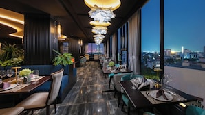 A modern restaurant with a long dining area, large windows, and a city view. - May De Ville Corner Hotel (Hanoi)